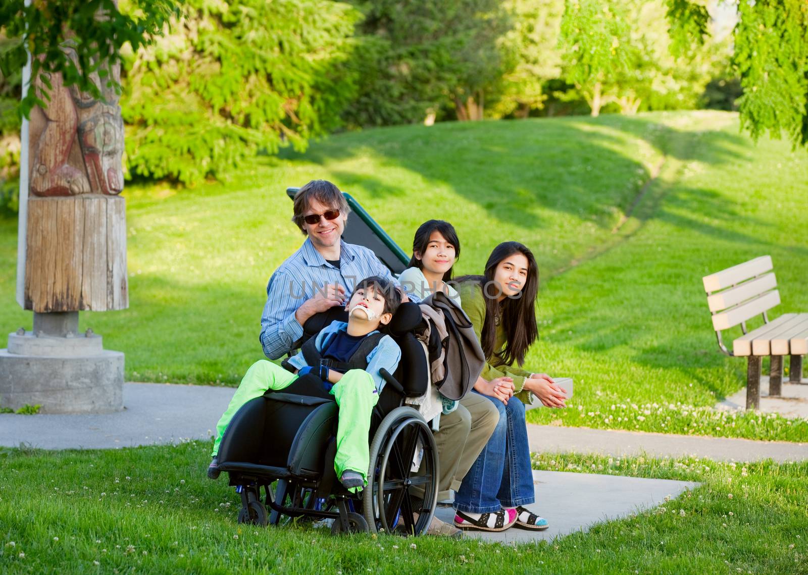 Disabled boy in wheelchair with family outdoors on sunny day sitting at a park