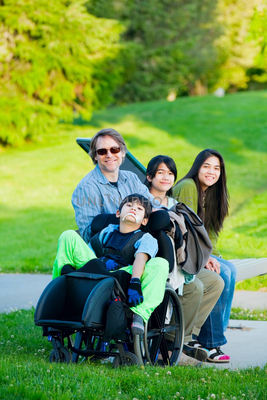 Disabled boy in wheelchair with family outdoors on sunny day sit by jarenwicklund