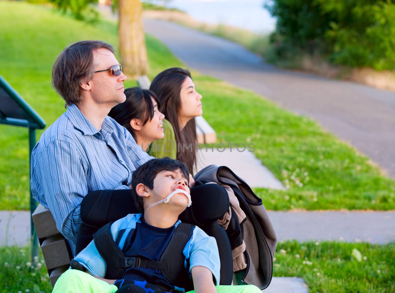 Disabled boy in wheelchair with family outdoors on sunny day sit by jarenwicklund