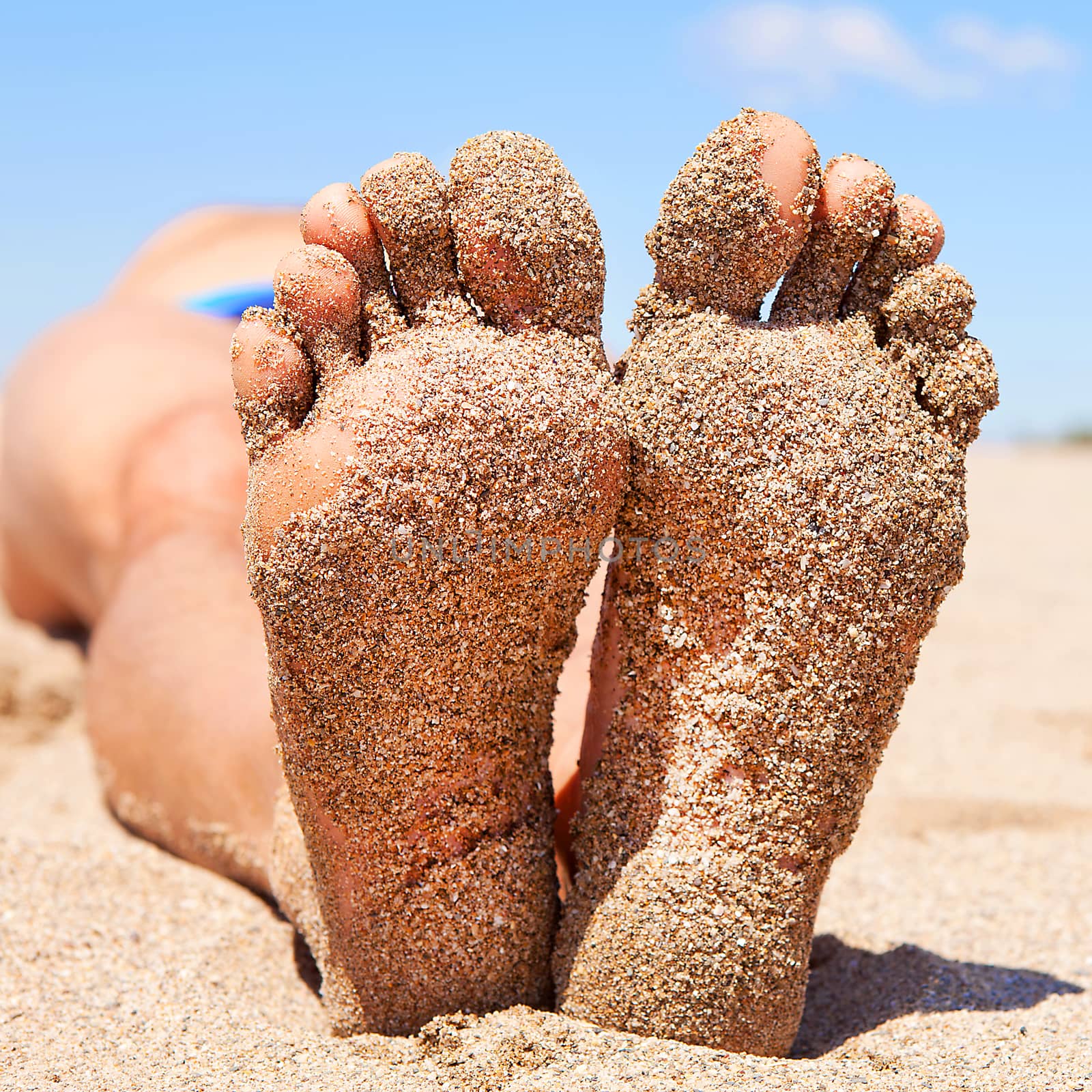 bottom of male feet covered with sand on the beach in sunshine