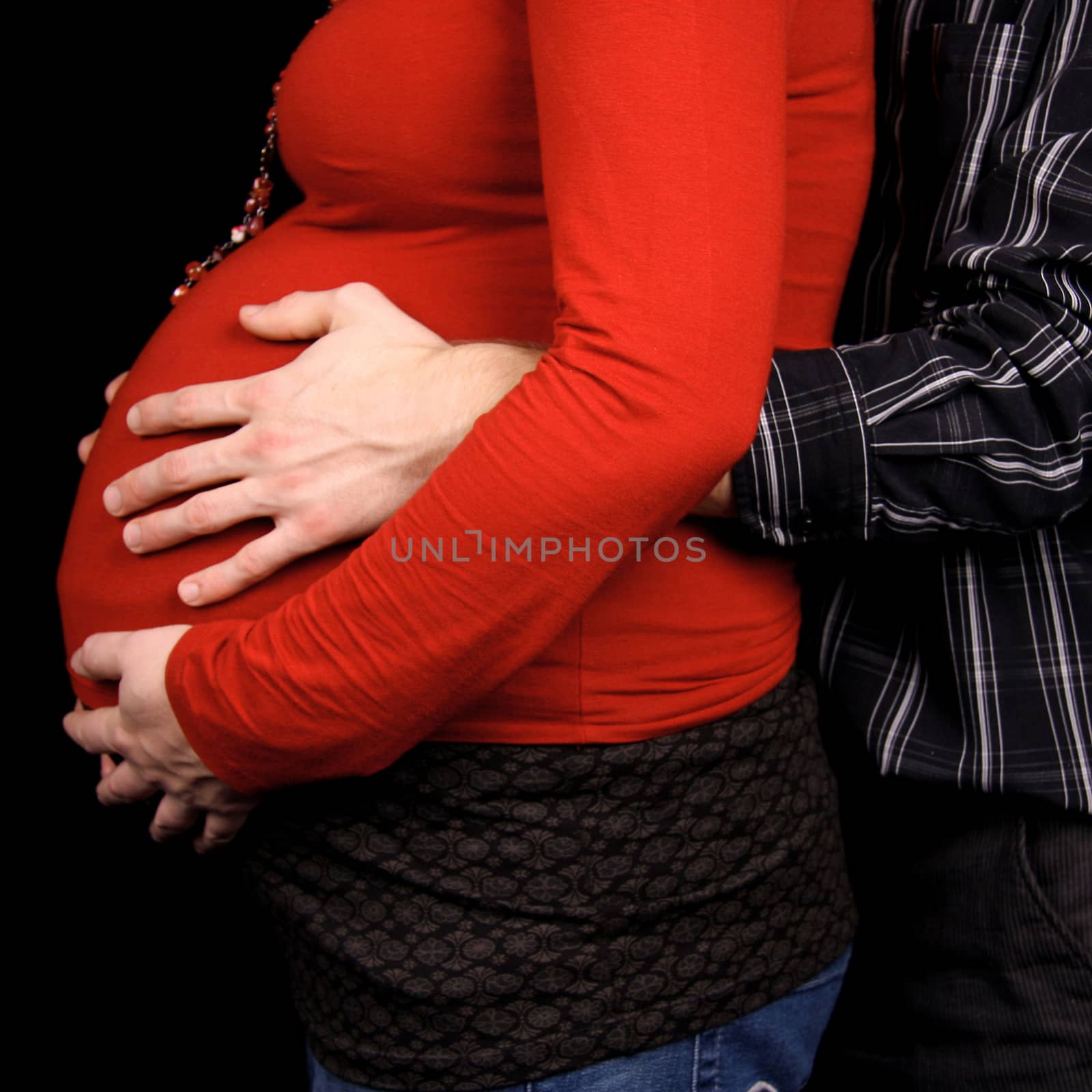 pregnant couple in closeup holding belly over black background