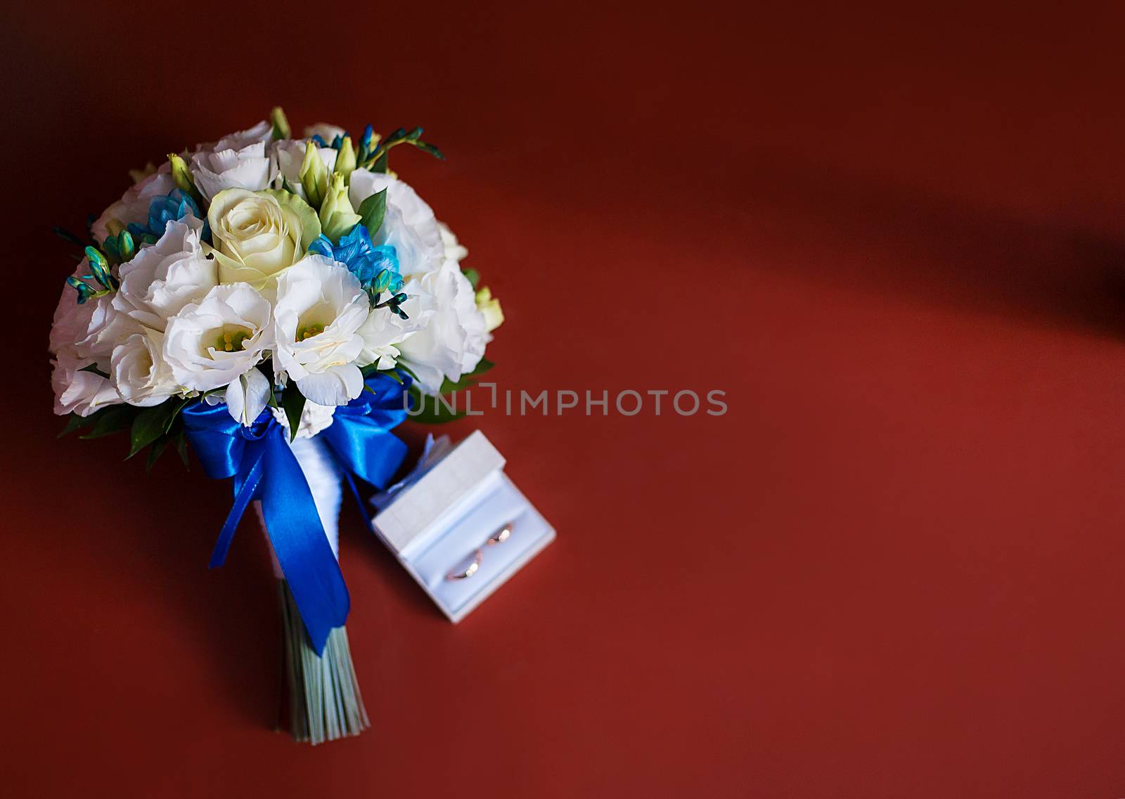 Wedding rings with a bridal bouquet of white roses on red