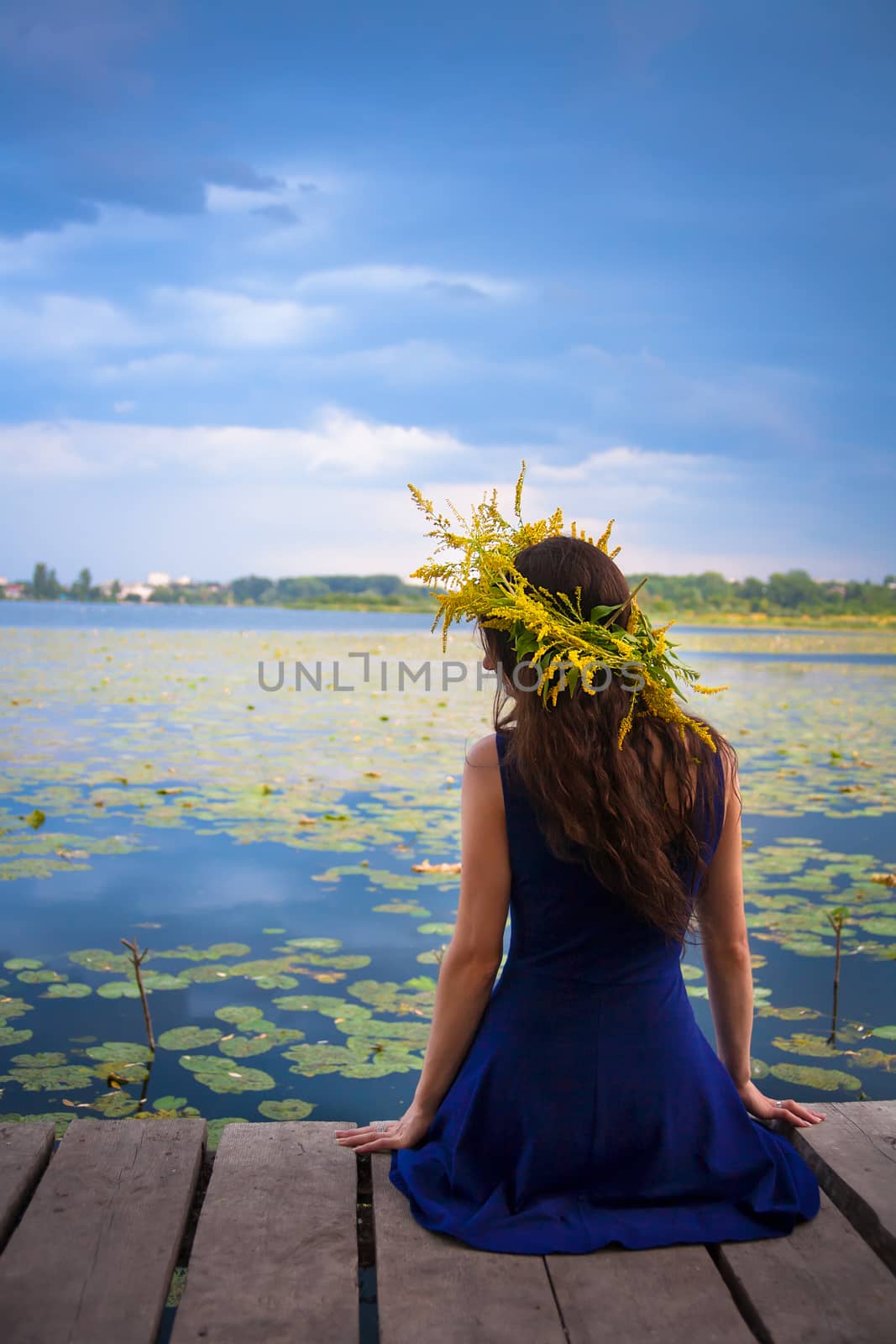 girl by the lake with a wreath on head. Blue sky. Back view