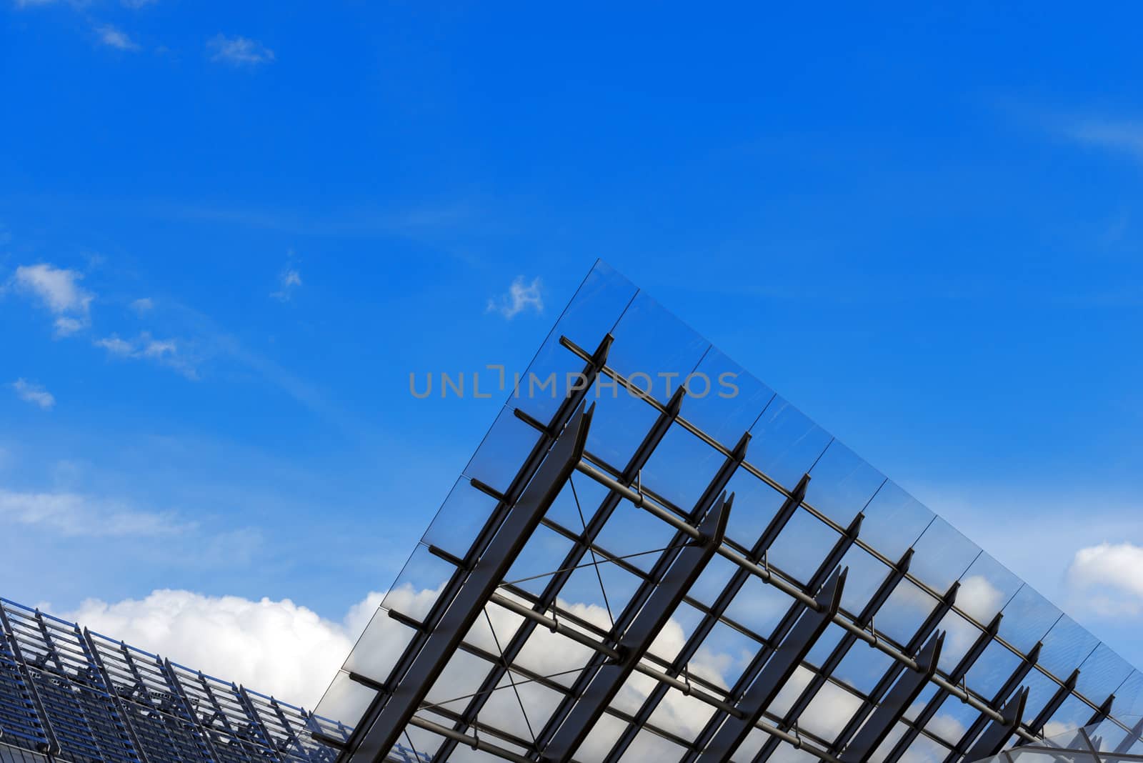 Detail of steel and glass roof of a modern building with blue sky and clouds