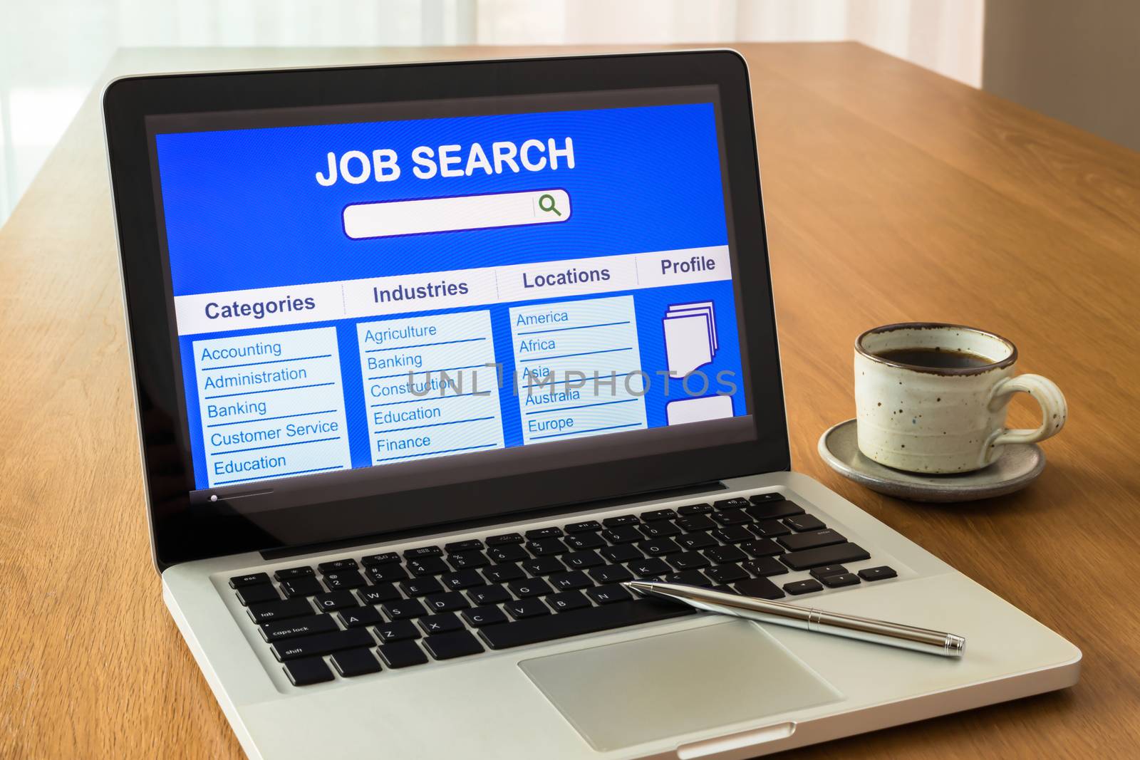 Laptop shows user interface of online job search on display screen and a cup of coffee on wooden desk, natural light coming through the window.