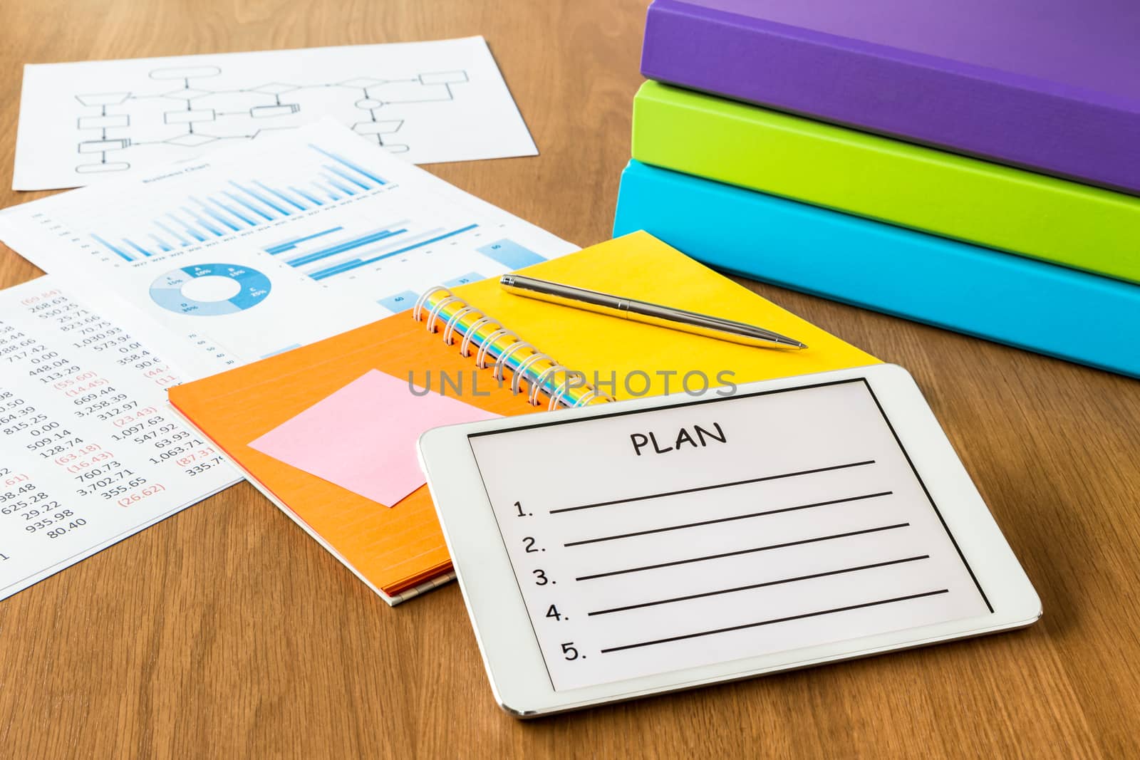 Digital tablet pc showing blank form of project planning on a display screen, colorful diary book, binders and documents on workspace