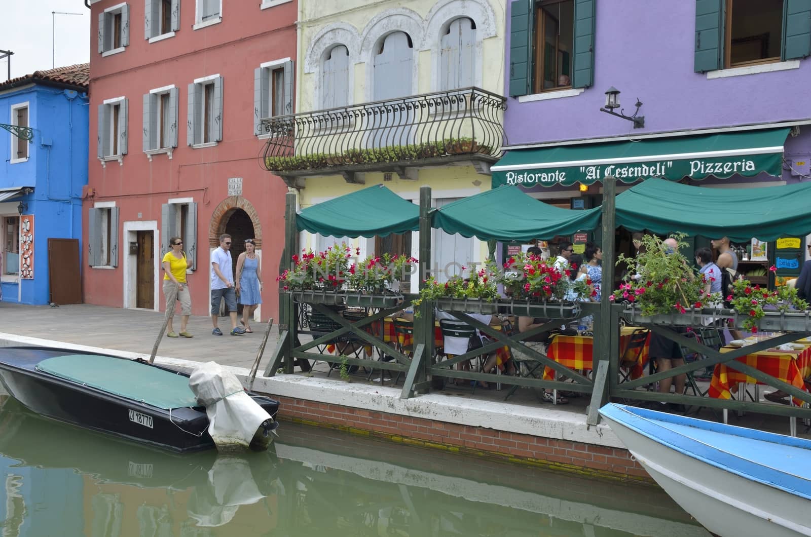 Some people walking by a way along a small canal in Burano, a colorful island of Venice, Italy