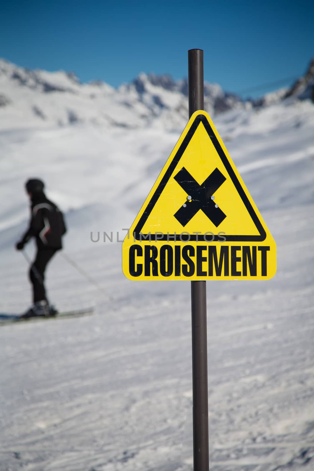 A skier passing by a sign of crossing slopes