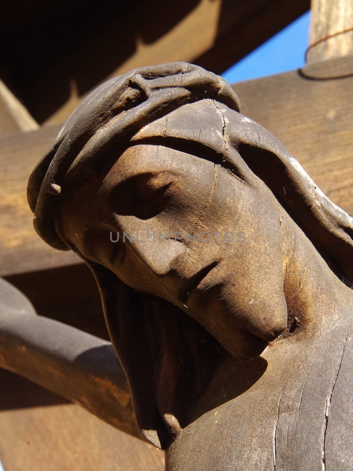 The wooden face of a carved Jesus as he hangs from the cross