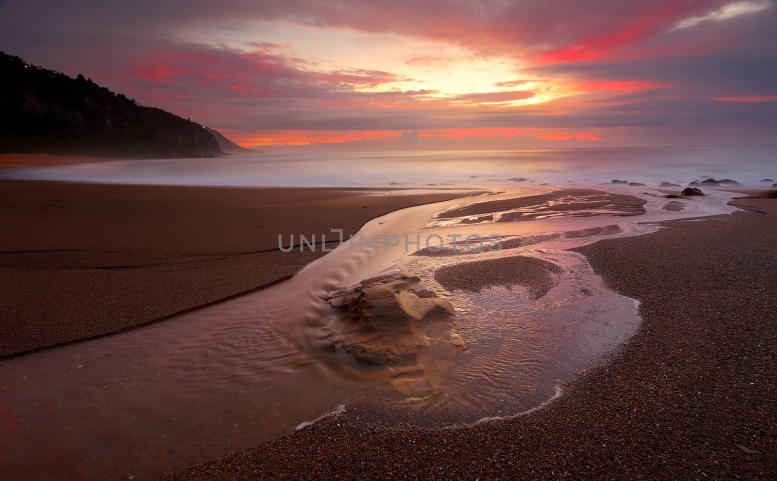 Long exposure at dawn as Stony Creek flows into the ocean, its waters capturing the light and colour of sunrise which contrasts against the still dark colours of the landscape.