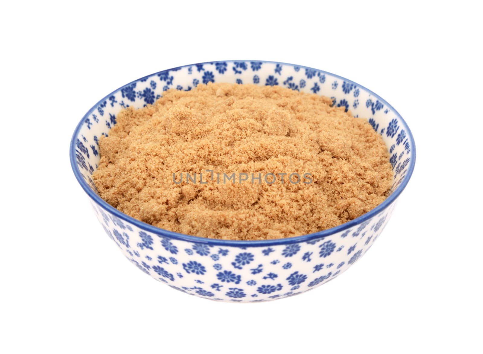 Light brown soft / muscovado sugar in a blue and white porcelain bowl with a floral design, isolated on a white background