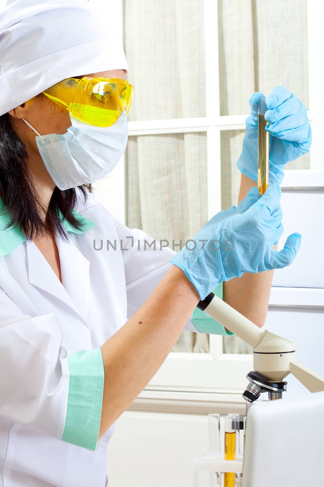 a female medical or scientific researcher or woman doctor looking at a test tube of yellow solution in a laboratory