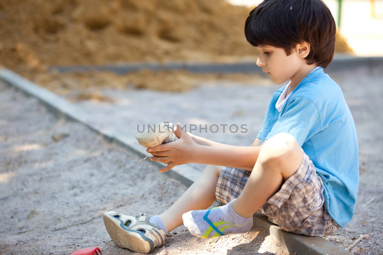 boy shakes the sand out of the shoe on the playground