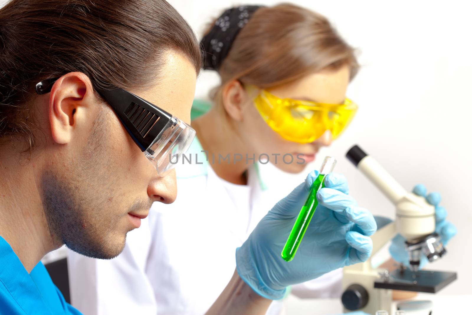 Male researcher analyzes tubes and his colleague looking through the microscope  