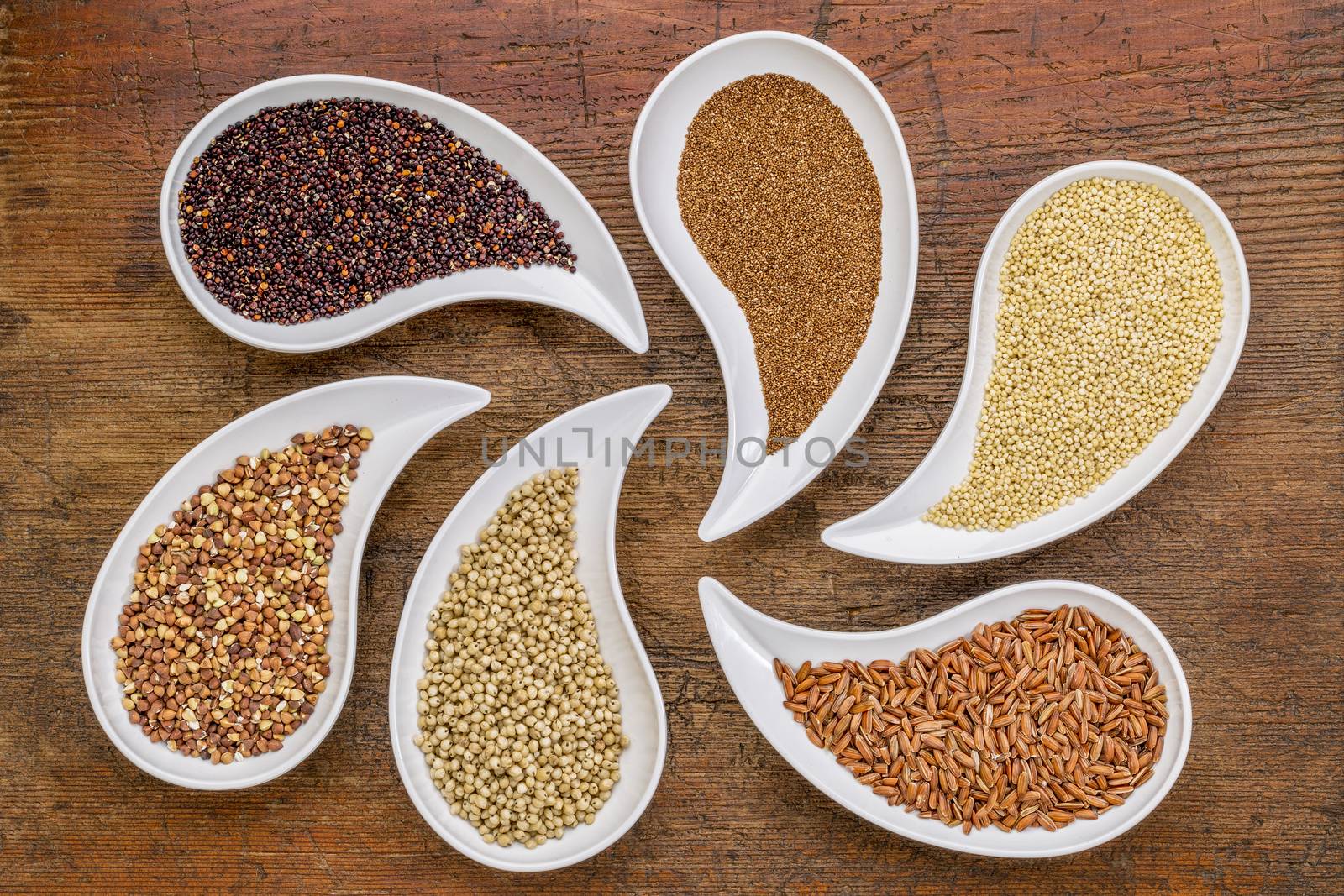 gluten free grain abstract - top view of teardrop shaped bowls with quinoa, teff, millet, rice, sorghum and buckwheat grains against grunge wood