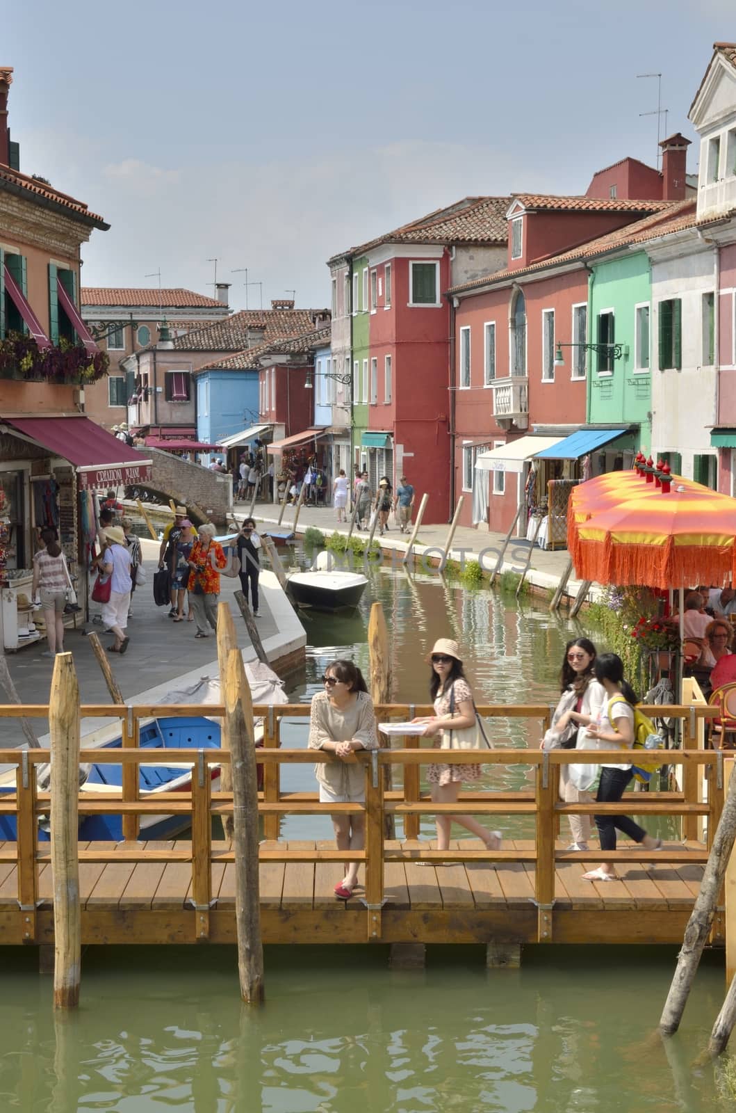 Some tourists on a wooden bridge over a canal  in Burano, a colorful island of Venice, Italy