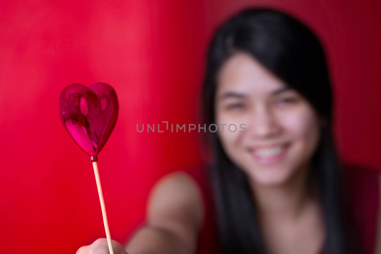 Beautiful biracial young teen girl holding heart balloon, smiling.