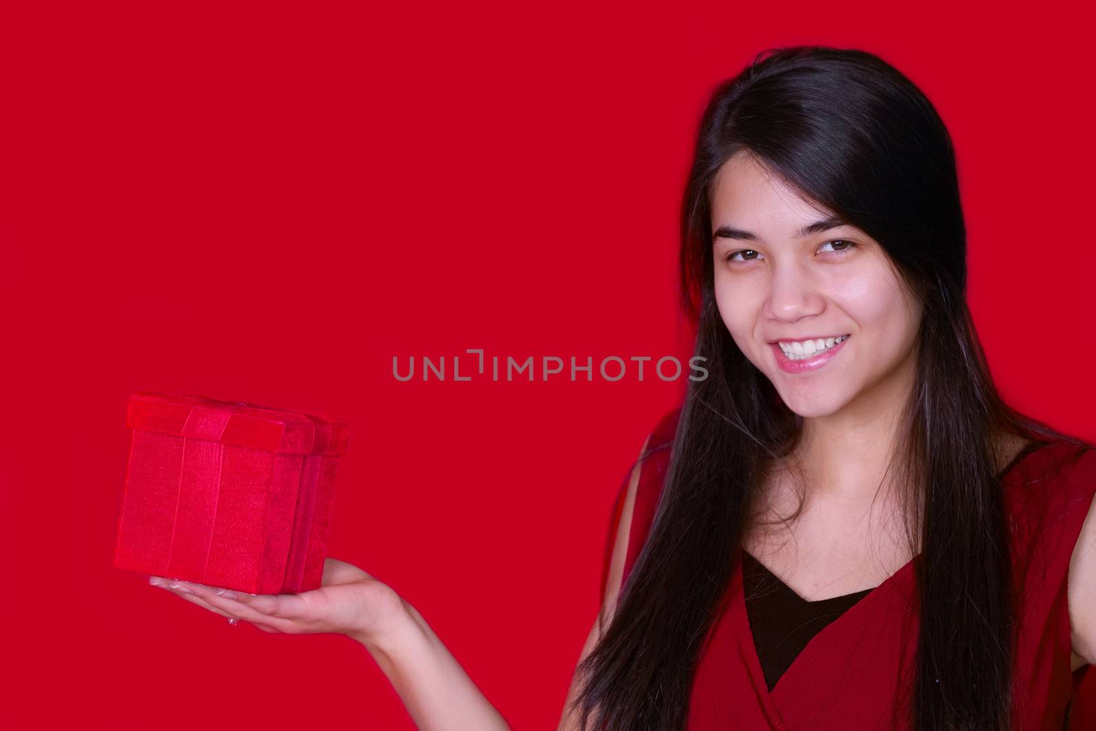 Beautiful biracial teen girl in red dress holding red present on red background