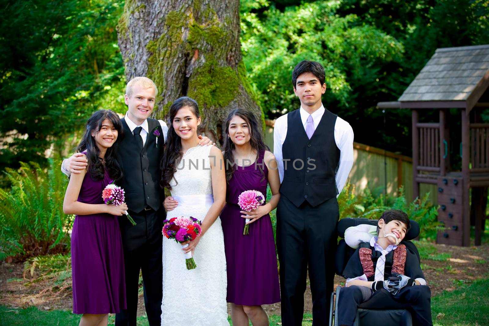 Interracial wedding. Groom standing with his biracial bride's brothers and sisters outdoors. Youngest boy is disabled with cerebral palsy.