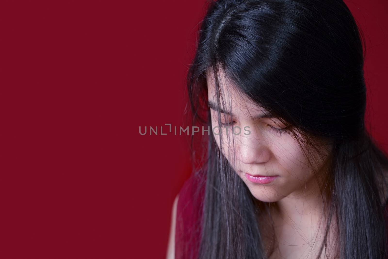 Beautiful, biracial teen girl looking down, depressed or sad, on red background