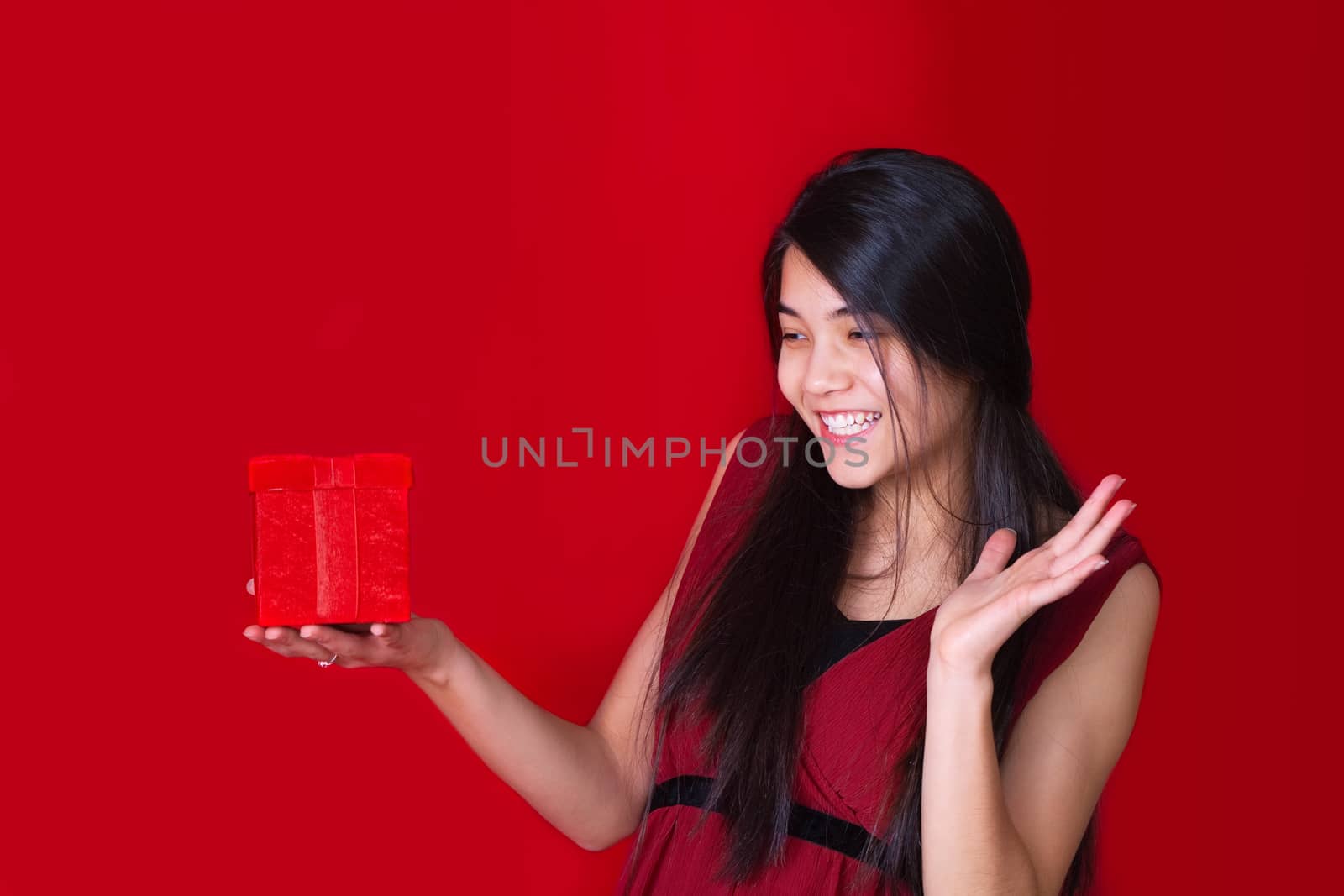 Beautiful biracial teen girl in red dress holding red present on by jarenwicklund