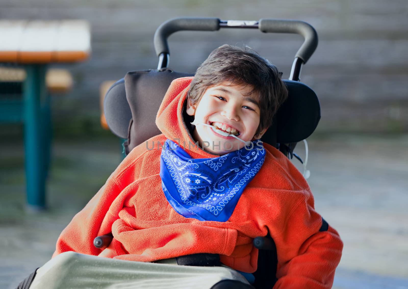 Handsome, happy biracial eight year old boy smiling in wheelchair outdoors