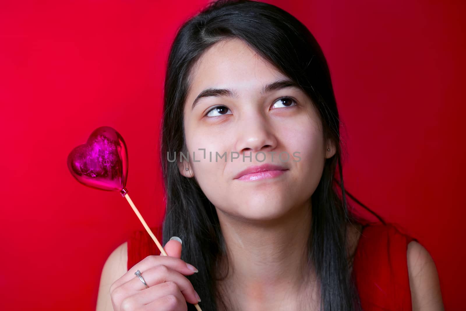 Beautiful biracial young teen girl holding heart balloon, smiling.