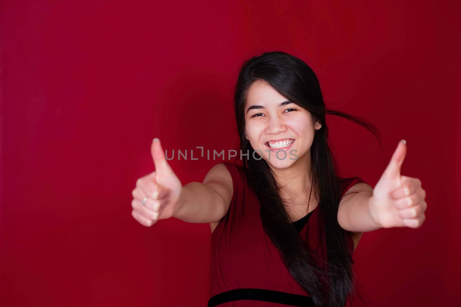 Beautiful biracial teen girl with thumbs up on red background by jarenwicklund