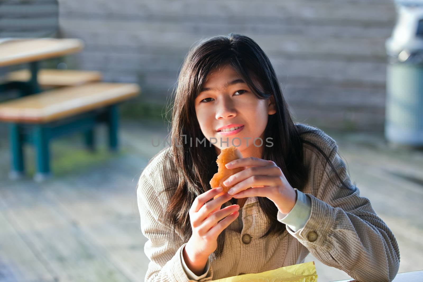 Young biracial teen girl outdoors eating hamburger by jarenwicklund