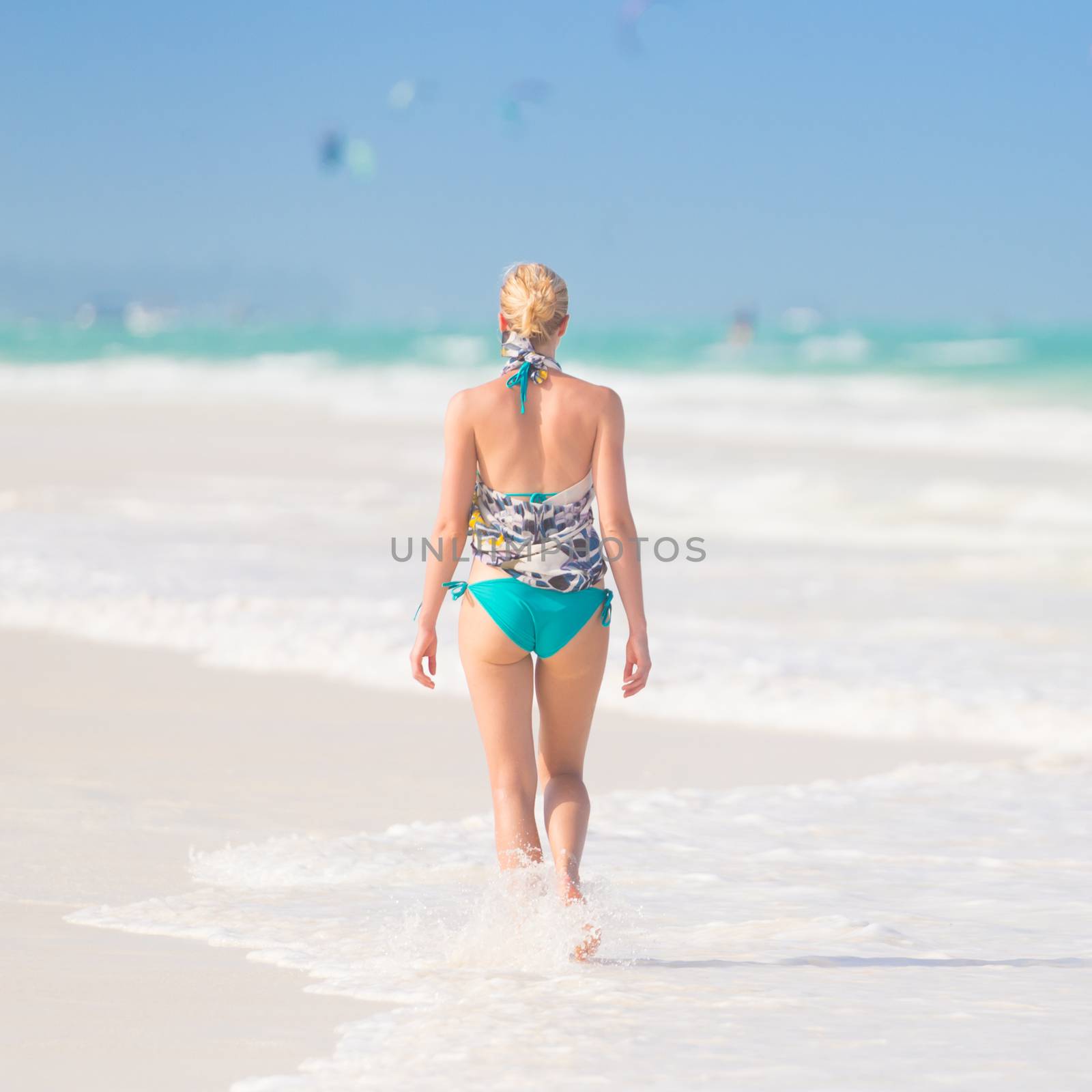 Happy woman having fun, enjoying summer, walking joyfully on tropical beach. Beautiful caucasian model  wearing colorful scarf and turquoise bikini on vacations on Paje beach, Zanzibar, Tanzania