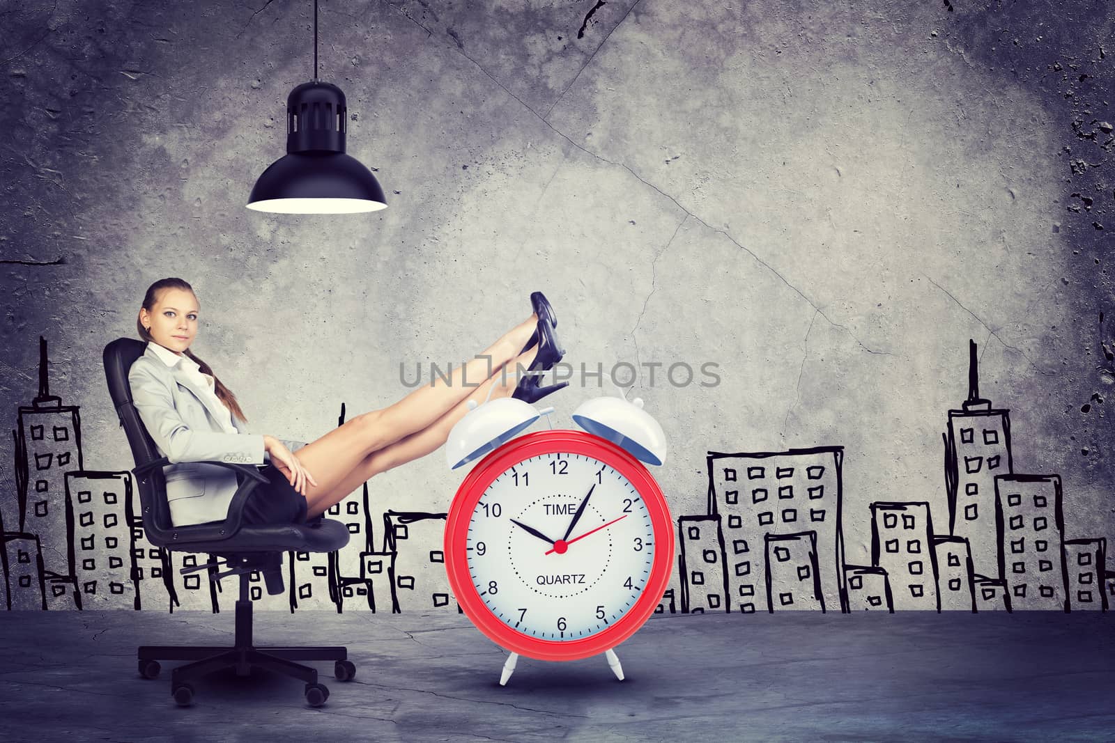 Businesswoman sitting in office chair with her feet up on alarm-clock, in front of raw concrete wall with sketch of city on it, looking at camera