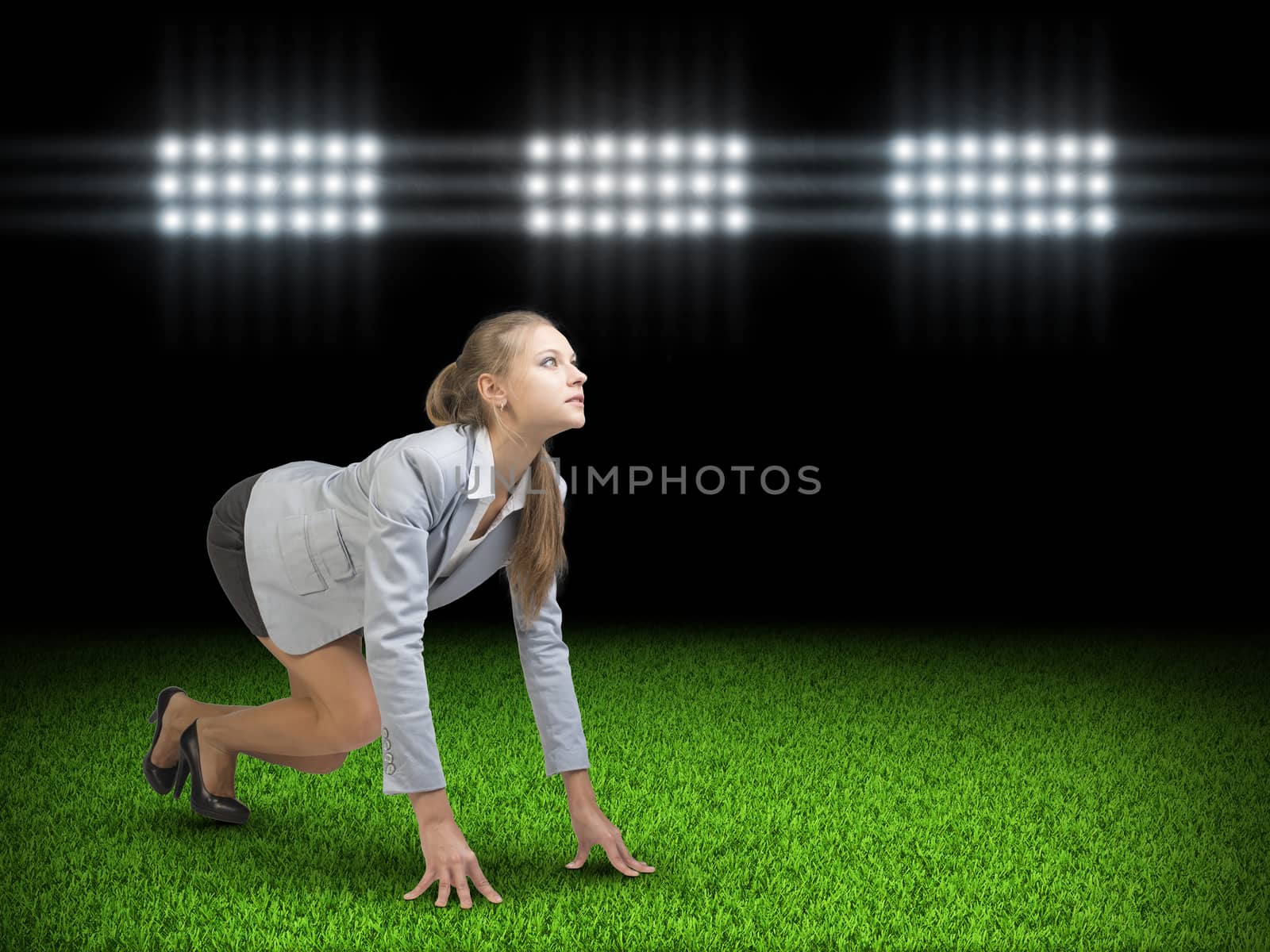 Businesswoman standing in running start pose at green grass court illuminated by spotlights, looking ahead