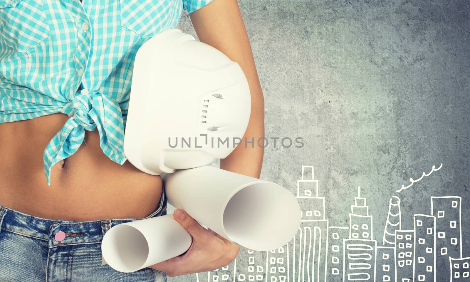 Close-up of woman holding hard hat and drawing rolls, against stone wall with sketch of city on it 