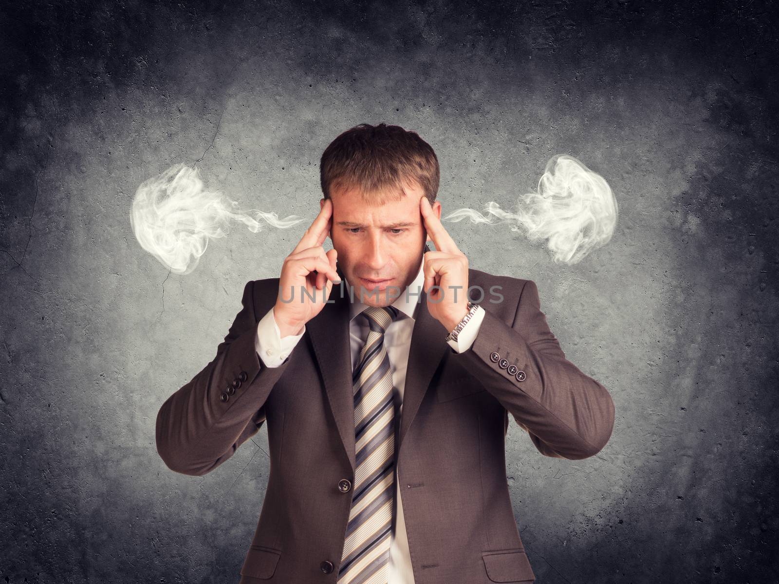 Stressed businessman thinking with his fingers on his temples, smoke from his ears. Raw concrete wall as backdrop