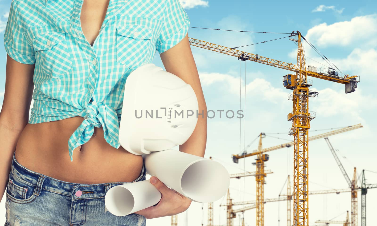 Close-up of woman holding hard hat and drawing rolls. Sky, clouds and tower cranes as backdrop