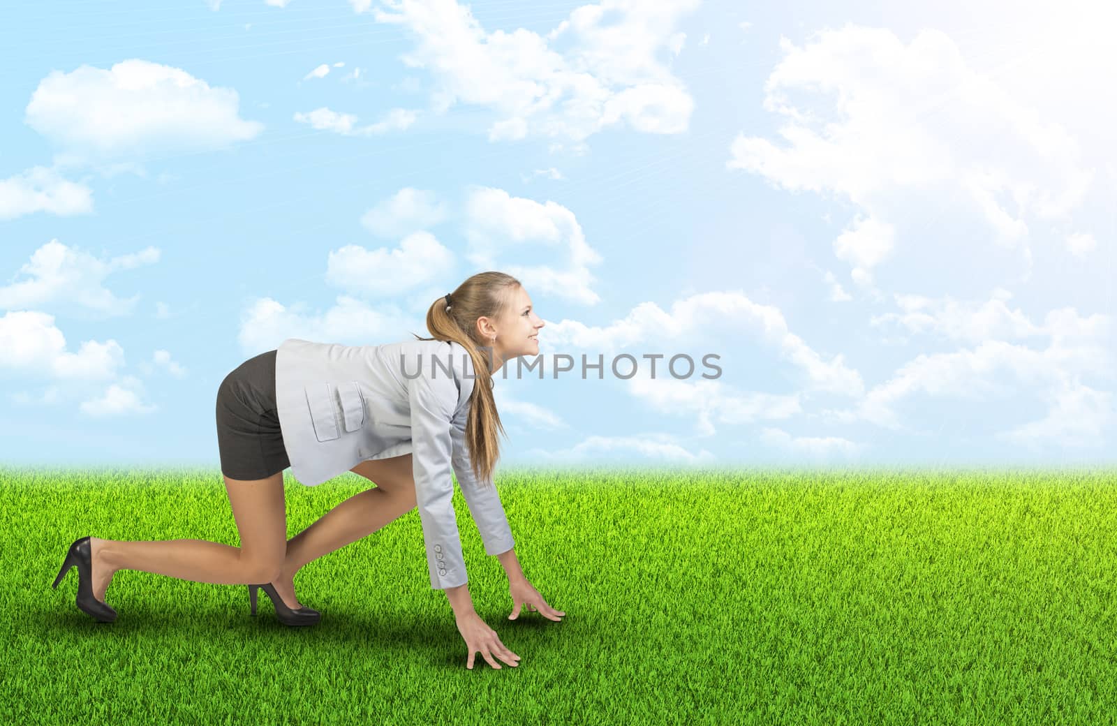 Businesswoman standing in running start pose at green field, looking ahead, smiling
