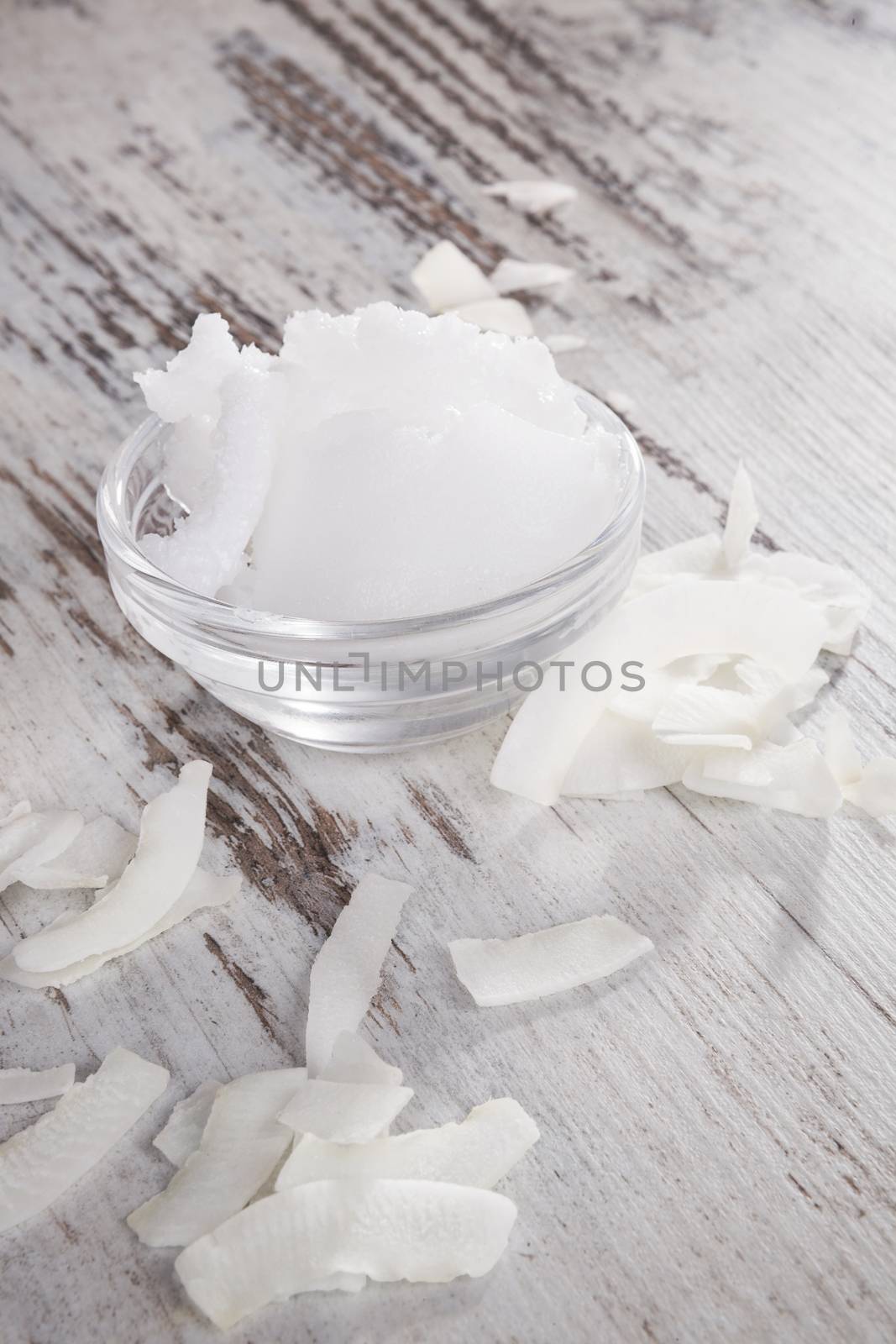 Coconut oil and coconut flakes on white textured wooden background. Healthy eating and cooking. 