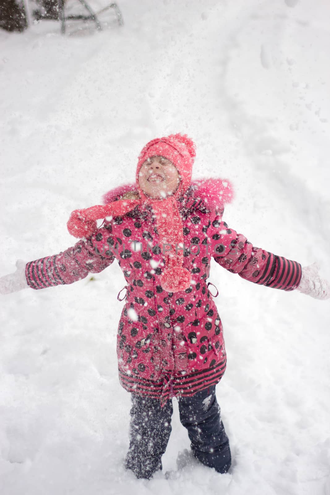 Little girl in winter pink hat in snow.