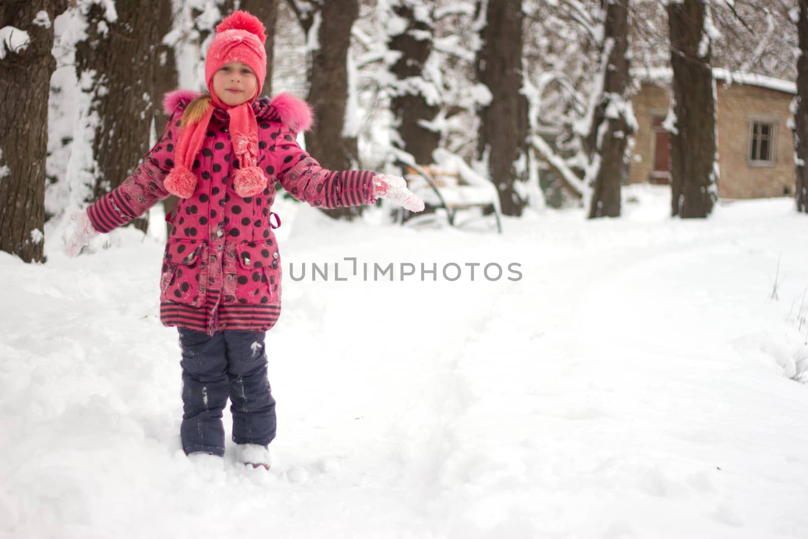 Little girl in winter pink hat in snow.