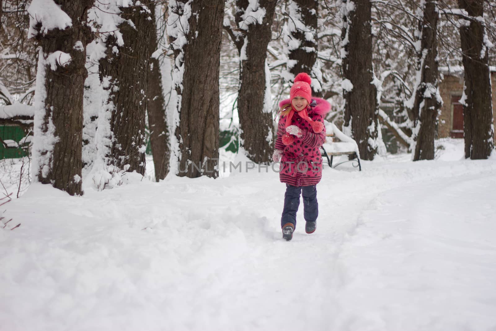 Little girl in winter pink hat in snow.