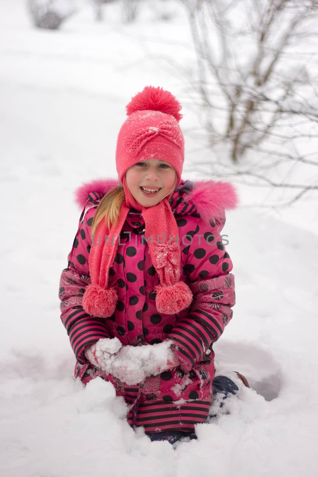 Little girl in winter pink hat in snow.