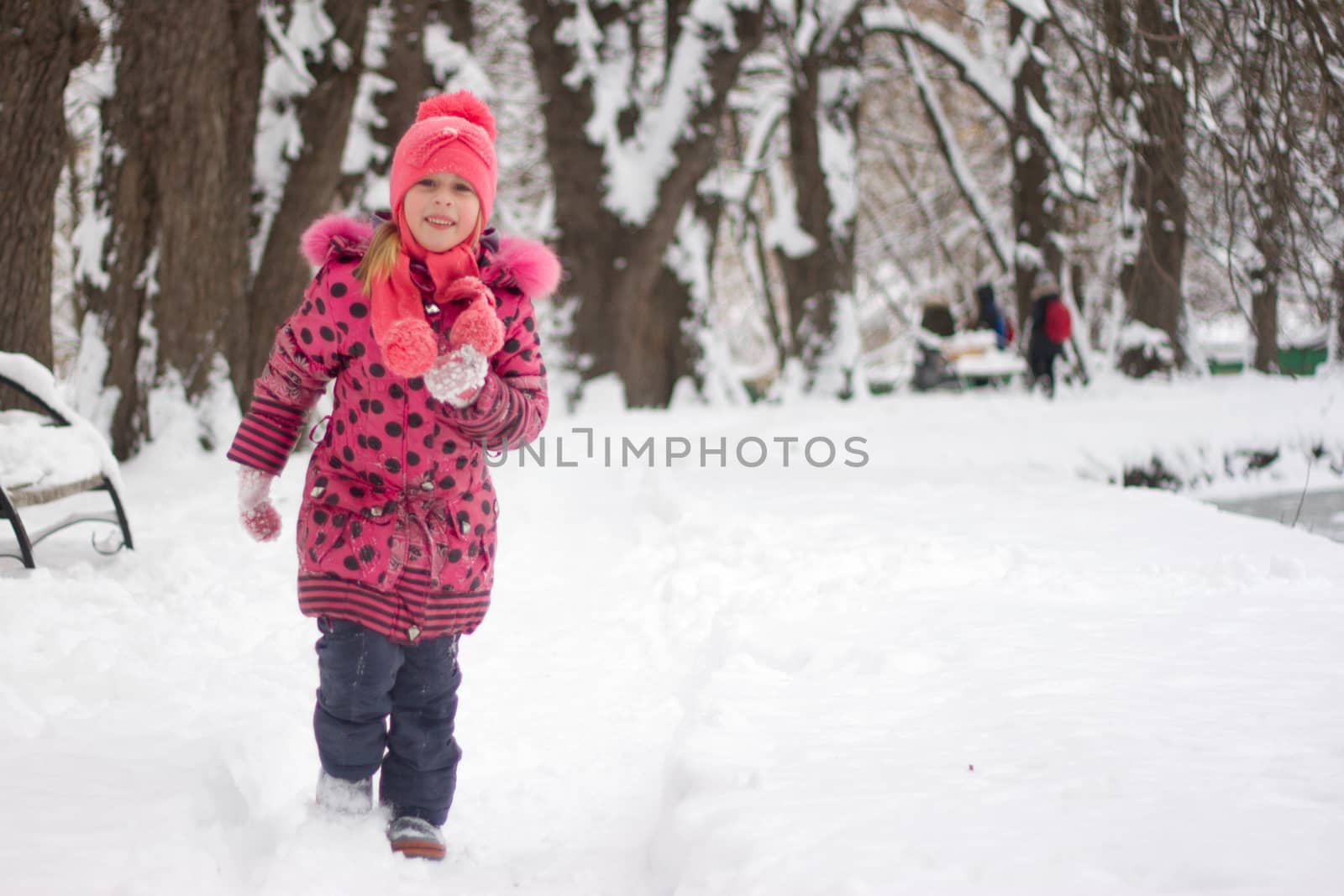 Little girl in winter pink hat in snow.