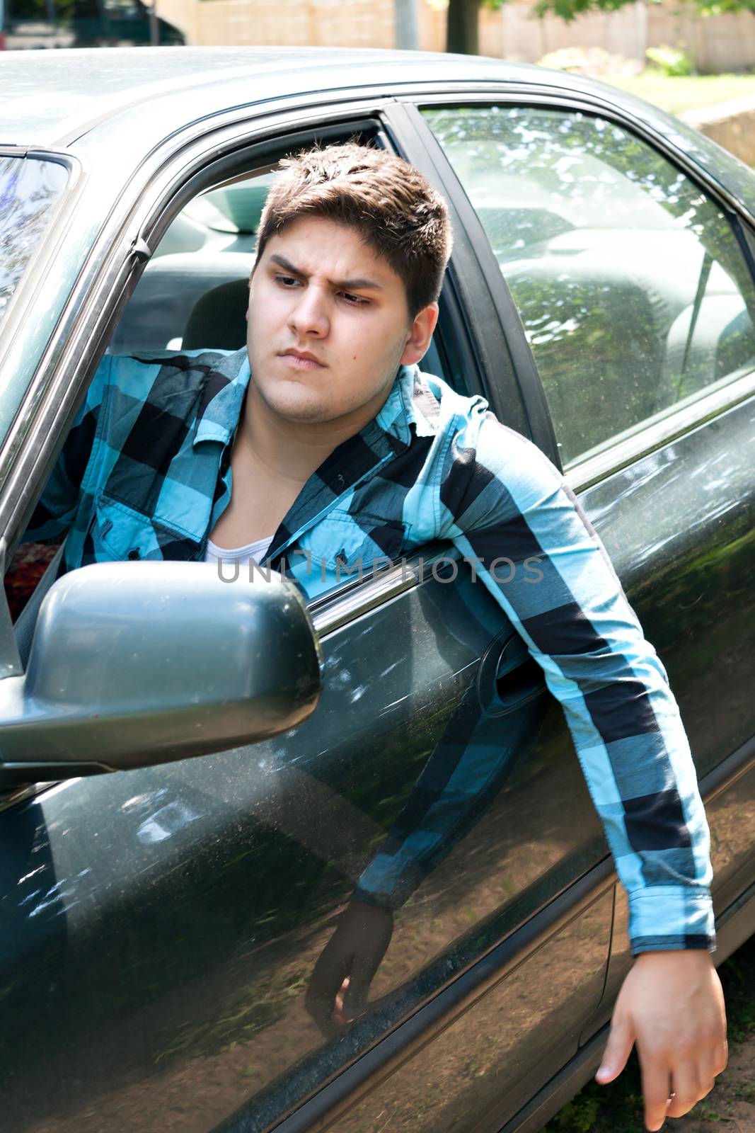 An irritated young man driving a vehicle with his head and arm hanging out of the window.