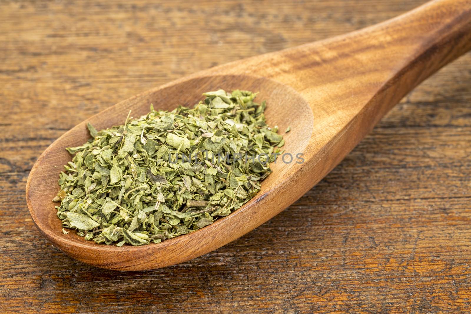 organic dried oregano leaf on a wooden spoon against a grunge wood background