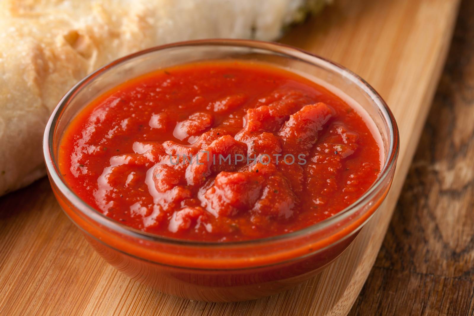 Freshly prepared pasta or pizza sauce marinara in a glass bowl. Bread in background.