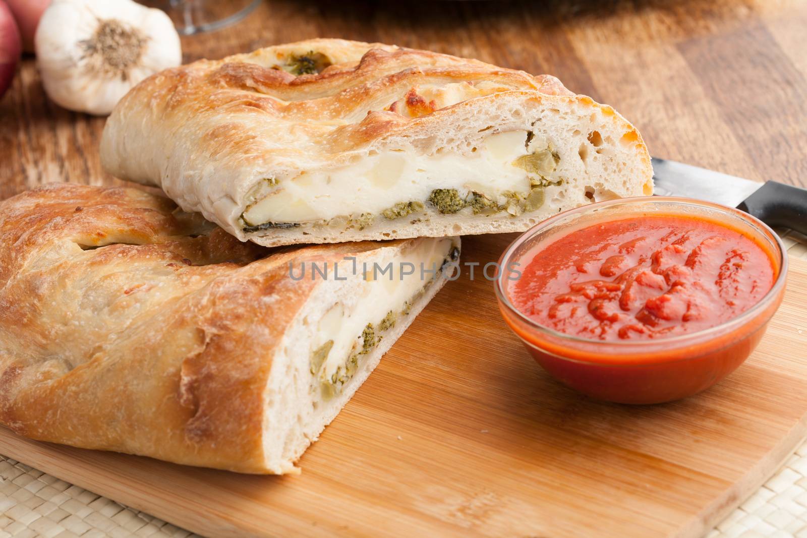 Homemade stromboli or stuffed bread with broccoli potatoes garlic onions and mozzarella cheese along with a side of marinara dipping sauce.