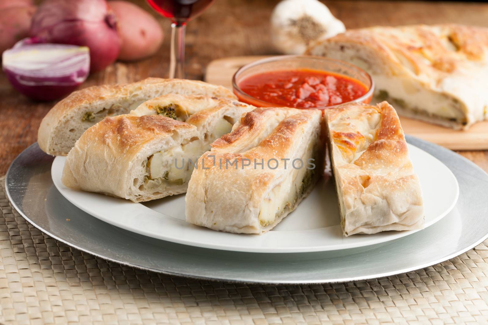 Homemade stromboli or stuffed bread with broccoli potatoes garlic onions and mozzarella cheese along with a side of marinara dipping sauce.