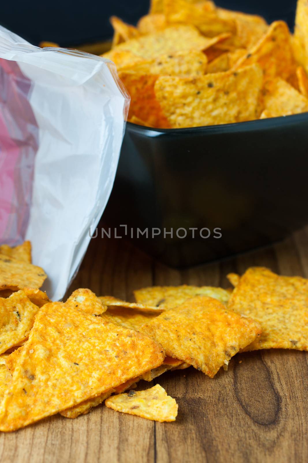 Nacho cheese flavored tortilla chips in a dark bowl on a wooden table.