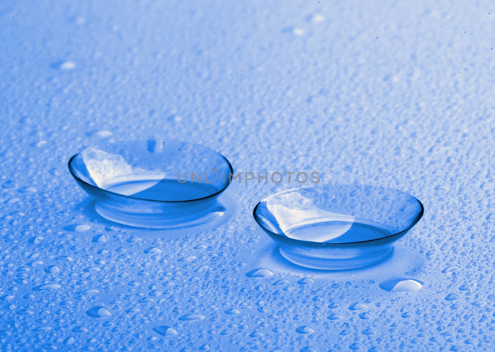 Two Contact Lenses with Water Droplets isolated on Wet background. Ultramarine Toned.