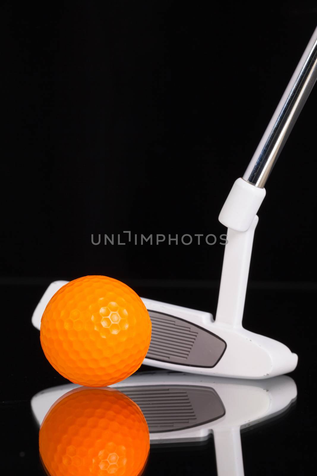 Golf putter and gold equipments on the black glass desk by CaptureLight